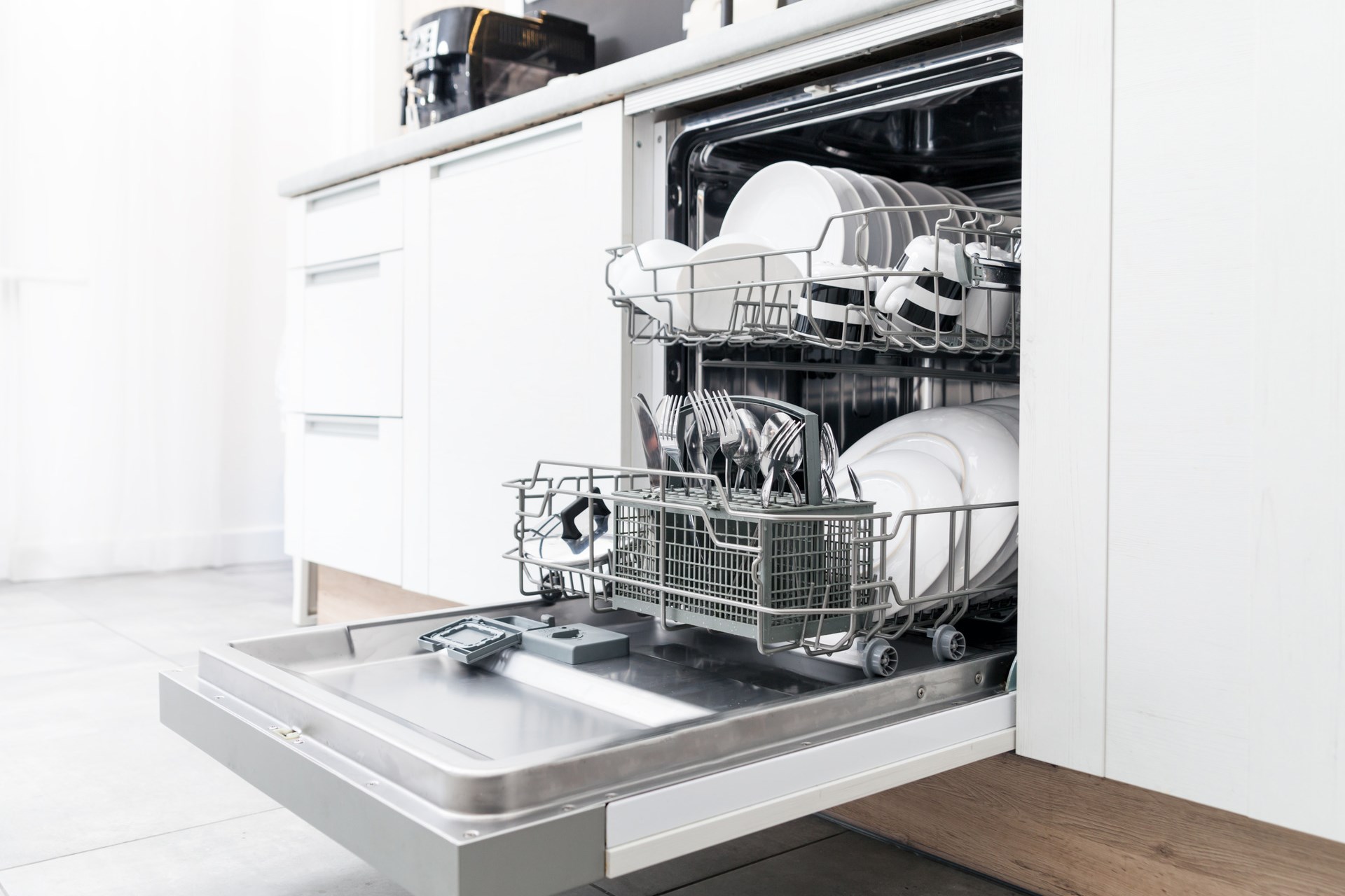 打开洗碗机用干净的菜肴在白色厨房里